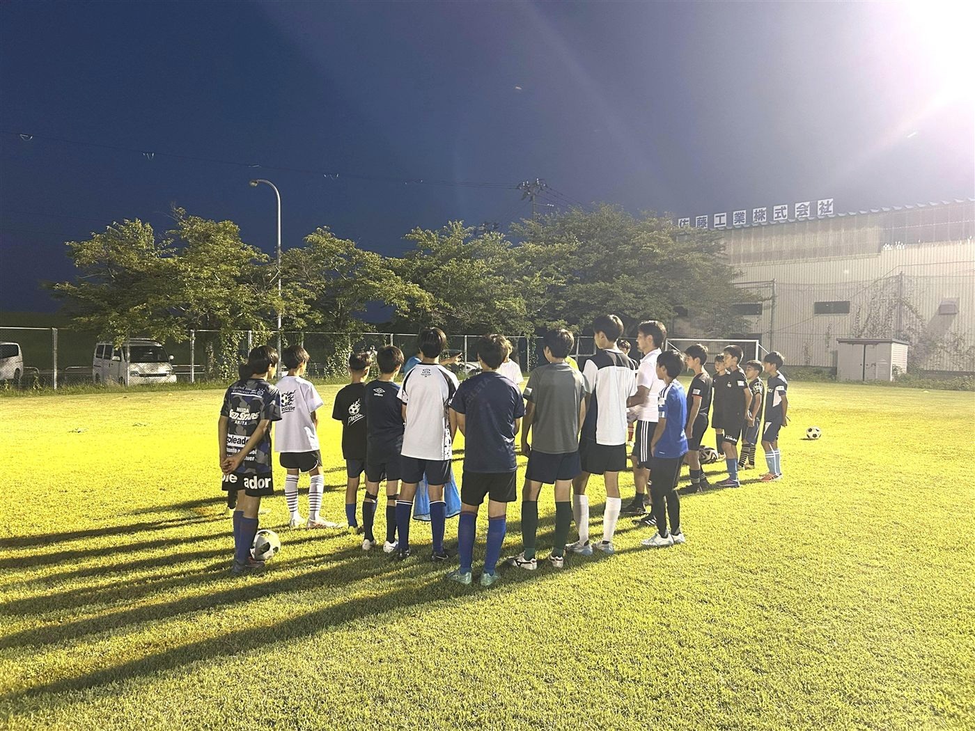 夜のグラウンドでコーチの話を聞く子どもたち